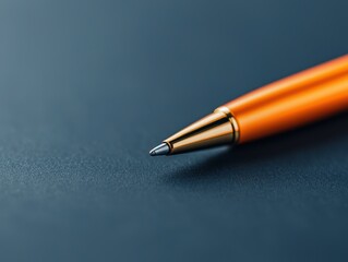 Close-up of an orange ballpoint pen tip resting on a textured dark surface.