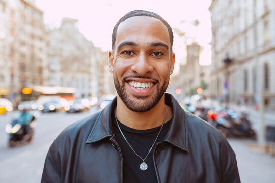 Close up portrait of a smiling multiracial young bearded tourist with braids, enjoying his trip to barcelona, looking at camera.