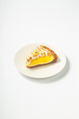 A slice of lemon meringue pie with a golden brown crust and toasted meringue topping, served on a simple white plate over a bright white background. Fresh and delicious dessert presentation.