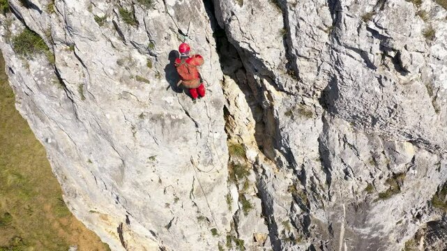 Aerial view of mountain rescuer rappelling on a rocky wall hanging on a rope