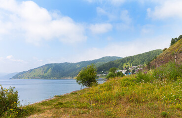 Obraz premium Beautiful landscape of coast of Baikal Lake. View of the village of Port-Baikal on the shore lake with flowers field on a sunny summer day. Circum-Baikal Railway station. Travel and outdoor recreation