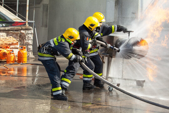 Firefighters work together using water hose to extinguish a dangerous fire during a training drill