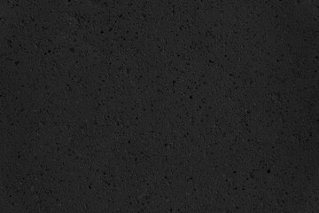 A black wall with a lot of small rocks on it. The wall is very plain.