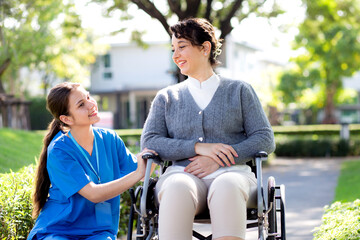 Young caucasian nurse comforting with patient while sitting on wheelchair in outdoor park, doctor woman support and counseling with patient, caregiver and service, medical and consoling.