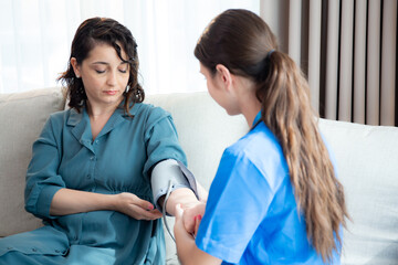 Obraz premium Caregiver caucasian young nurse woman measuring blood pressure with patient for checkup pulse health and examining in living room at home, nurse checkup patient for health care, medical and insurance.