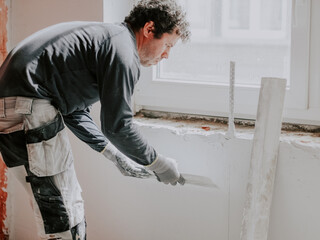 A young man is putting putty on the wall.