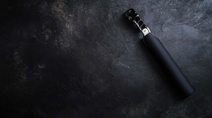 Naklejka premium Sleek black umbrella with chrome handle on a textured dark surface.