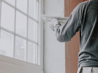A young man is putting putty on a window opening.