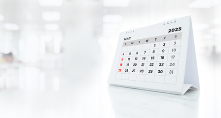 May 2025 desk calendar on white marble table on blurred office background.