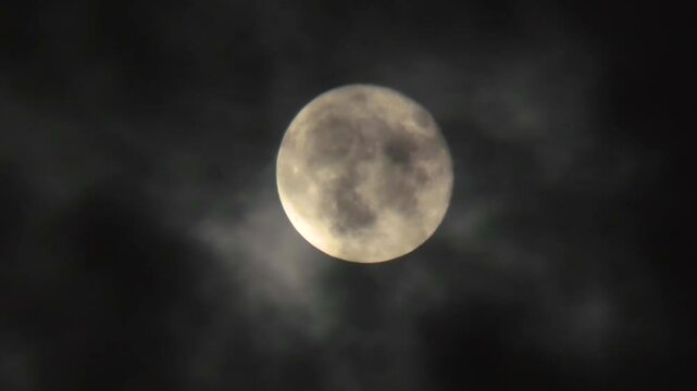 Clouds fly in front of the moon in the night sky. Full moon close-up and cloudy dark sky. Real shot through a telephoto lens