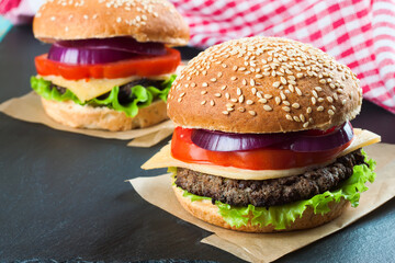 Homemade cheeseburger on black slate surface.