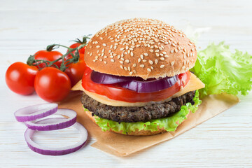 Homemade cheeseburger on white wooden surface.