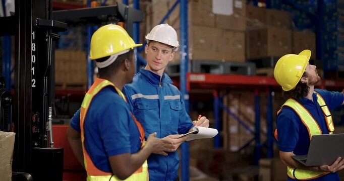 Male engineers from different ethnic backgrounds standing together in warehouse environment reviewing notes and data to ensure accuracy and progress of warehouse operation as a collaborative task