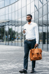 A man in formal clothes with a briefcase in one hand and a disposable cup of coffee in the other...