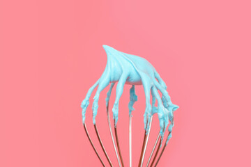 Whisk with blue whipped cream from proteins close-up on pink background.