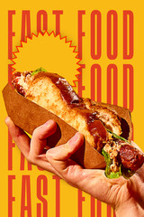 Hand holding delicious hot dog sandwich with grilled sausage, salad and bun on bold yellow...