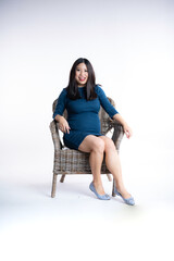 Fototapeta premium Happy pregnant mother standing beside wicker chair while smiling toddler boy sitting playfully showing tongue in cozy studio setup concept of maternity family love second child anticipation