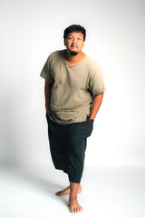 Fototapeta premium Portrait of an Asian Thai man with casual clothes standing barefoot on white background, showing relaxed attitude, natural confidence, cultural identity, and authentic lifestyle in studio shot
