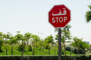 A red stop sign displaying text in both Arabic and English stands prominently against a lush green...
