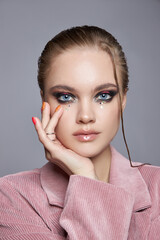 model poses elegantly in a studio, displaying unique makeup featuring bold eyes and glossy lips....