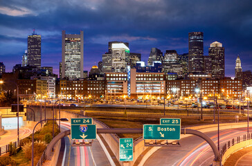 A stunning nighttime view of Boston’s illuminated skyline with bright highway lights and dramatic clouds creating a vibrant urban atmosphere.