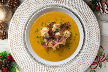 Pumpkin and cauliflower cream with crispy ham. Top view table with christmas decorations.
