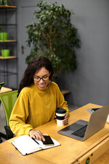 Beautiful young woman focused on work while sipping coffee in a modern office environment