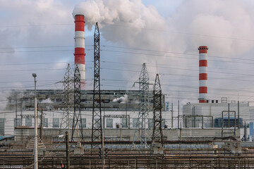 Large factory chimneys emit smoke into the atmosphere. Industrial zone and enterprises. View of industrial buildings and power lines. Plants and ecology. Thick smoke billows from factory chimneys.