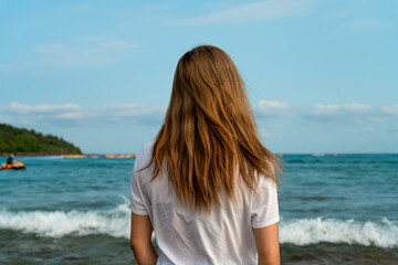 young woman standing on the beach looking out at horizon
