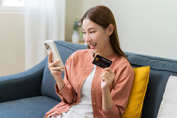 Bill pay, shopping order online internet, cute asian young woman hand holding credit card and mobile smart phone on sofa at home, female using banking service to secure payment with purchase on store.