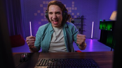 Young adult man spending time at home, man streamer gamer sits at desk with computer, streaming online and winning game, screaming winning expression. Person pov. © kinomaster