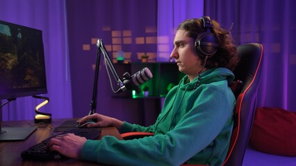 Young adult man spending time at home, man streamer gamer sits at desk with computer, streaming...