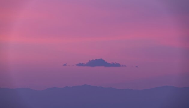 The gradient sky transitioned from a soft pink hue near the horizon to a deep purple at the zenith, with a single fluffy cloud leisurely drifting in the middle