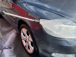 Close-up of car wash process. Man directing hose with water stream to his car, washing car at car...