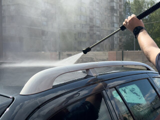 Close-up of car wash process. Man directing hose with water stream to his car, washing car at car...