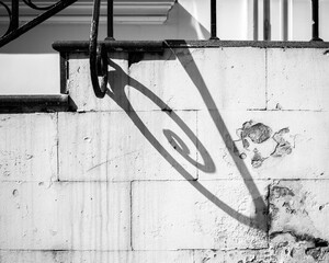 black and white photo, play of shadows with forged railing elements. shadow on a white stone wall