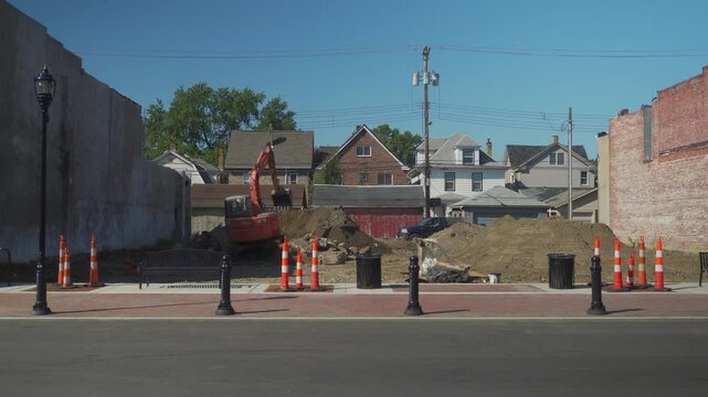 A backhoe clears dirt from an empty lot along the Main Street of a typical middle-American small town. Homes in the background. Pittsburgh suburbs.  	