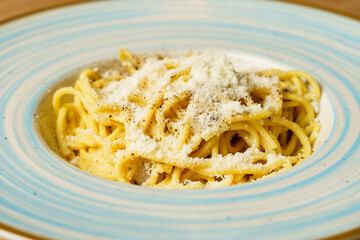 Classic spaghetti cacio e pepe with grated cheese on a blue-striped plate