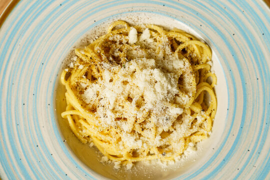 Classic spaghetti cacio e pepe with grated cheese on a blue-striped plate