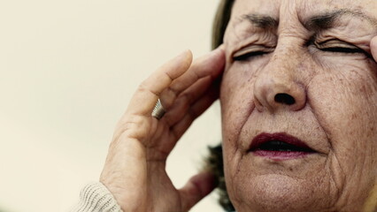 Elderly woman massaging her temples with eyes tightly shut, intense focus on relieving pain or...