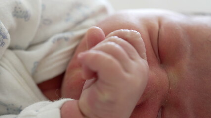 Close-up of a newborn baby gesticulating in sleep, with tiny hand movements and a slight grimace on...