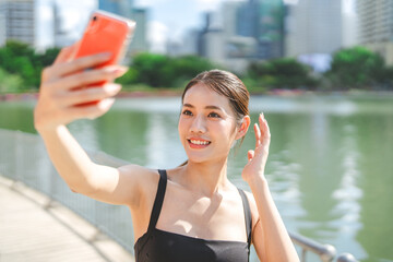 Young adult asian sport woman using smartphone selfie social media rest from running at outdoors