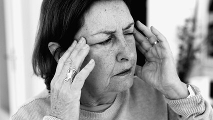 Elderly woman struggling with severe headache, massaging temples with visible concentration. Facial...