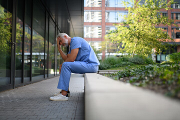Frustrated and burnt-out doctor sitting outside the hospital, feeling down.