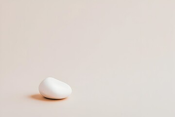 A smooth, off-white pebble rests on a pale backdrop  Minimalist composition