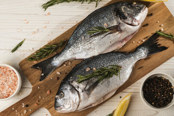Fresh dorado fish with lemon, rosemary and spices on wooden cutting board, close up