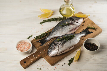 Fresh dorado fish with lemon, rosemary and spices on wooden cutting board, close up