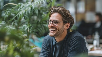 Obraz premium A young professional sitting in front of an indoor plant at his workplace, smiling.