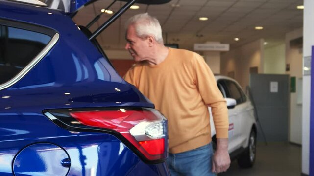 Senior man excitedly opens car trunk at the dealership