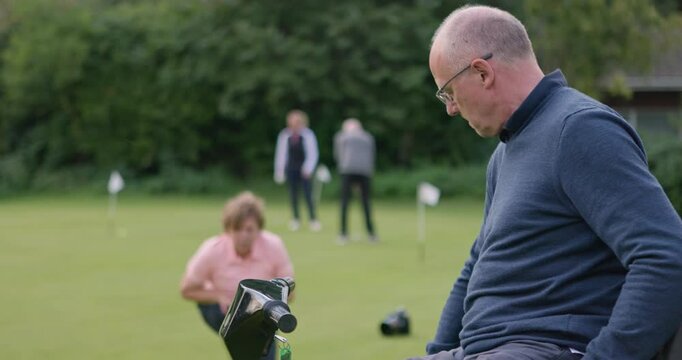 Sports, golf and an old man with a disability playing a game on a course green for leisure hobby. Fitness, recreation and a senior person taking a shot in a mobility scooter with a woman for support